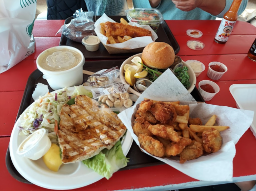 A colorful meal featuring grilled chicken, fried seafood, a burger, fries, salad, and various sauces on a tray.