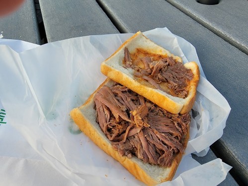 A sandwich with two slices of bread filled with shredded beef, resting on a piece of white paper on a wooden table.