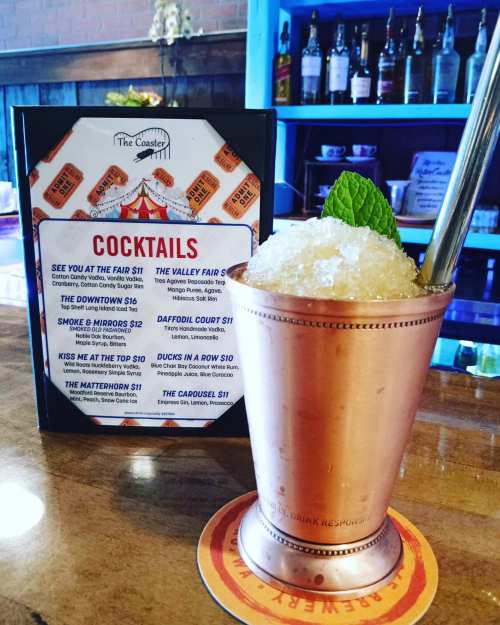 A copper cup filled with a mint garnish and crushed ice, next to a cocktail menu featuring various drink options.