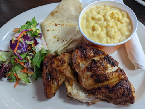 A plate with grilled chicken, macaroni and cheese, flatbread, and a side salad with mixed greens and shredded vegetables.