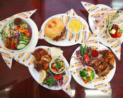 A spread of various dishes including grilled chicken, salad, a burger, macaroni, and fruit, all on branded plates.