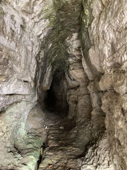 A narrow, rocky cave with textured walls and a dark passage leading deeper inside.