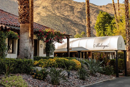A charming restaurant with a canopy, surrounded by lush greenery and mountains in the background.