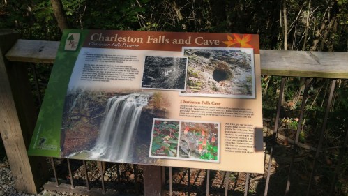 Sign for Charleston Falls and Cave, featuring images of the waterfall and cave, surrounded by trees.