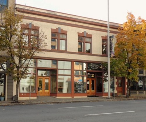 Historic building with large windows and decorative trim, surrounded by trees, on a city street.