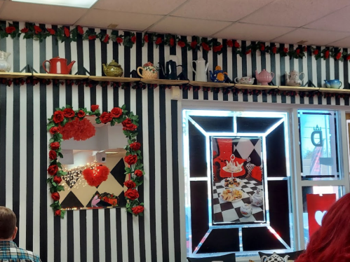 A whimsical café interior with black and white striped walls, decorated with teapots, roses, and playful artwork.