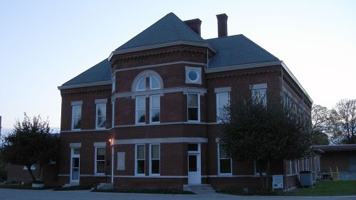 Historic brick building with a steep roof, large windows, and a well-maintained exterior, set against a twilight sky.