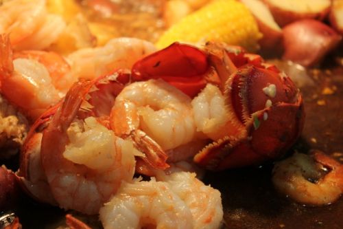 A close-up of a seafood dish featuring shrimp, lobster, corn, and potatoes in a savory broth.