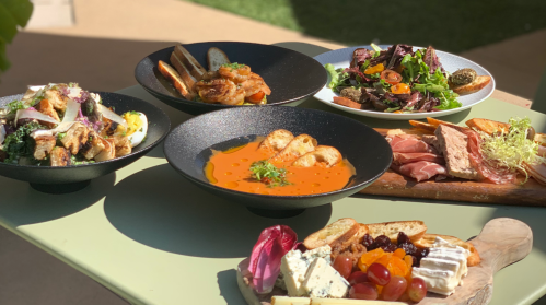 A variety of dishes including salads, seafood, and a cheese platter, beautifully arranged on a table outdoors.