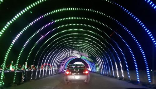A car drives through a colorful, illuminated tunnel of lights in various shades of green, blue, and purple.