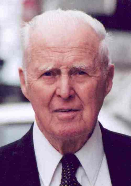 An elderly man with white hair and a suit, looking directly at the camera with a neutral expression.