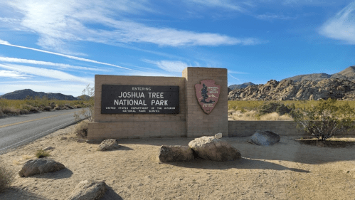 Sign marking the entrance to Joshua Tree National Park, surrounded by desert landscape and rocky formations.