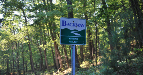 Sign for "Backway Mountain Parkway" surrounded by lush green trees in a forested area.