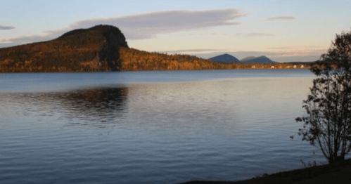 A serene lake at sunset, reflecting mountains and trees with autumn colors under a clear sky.