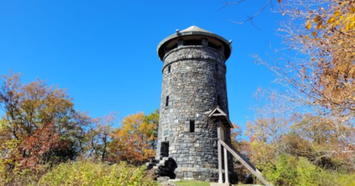 A tall stone tower surrounded by colorful autumn trees under a clear blue sky.