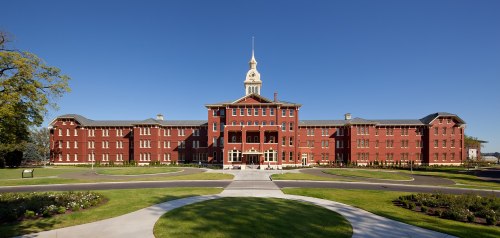 Historic red brick building with a central clock tower, surrounded by green lawns and clear blue skies.