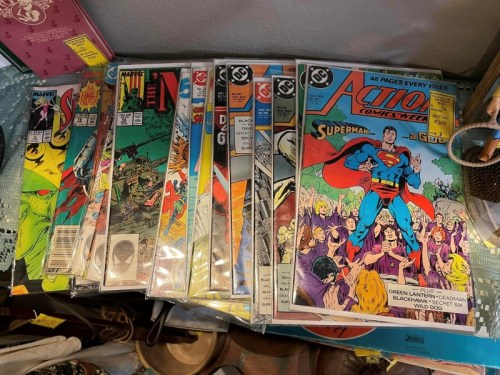 A collection of comic books featuring superheroes, including Superman, stacked on a table.