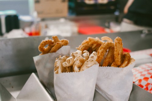 A variety of fried snacks in paper cones, including curly fries and onion rings, displayed on a counter.