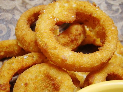 A close-up of golden, crispy onion rings piled on a plate, with a small bowl for dipping.
