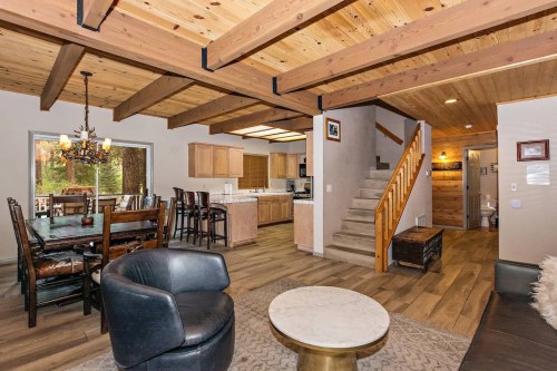Cozy living space with wooden beams, dining area, kitchen, and staircase, featuring modern decor and warm lighting.