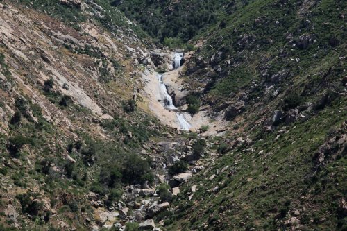 A scenic view of a rocky valley with a waterfall cascading down the hillside, surrounded by greenery.
