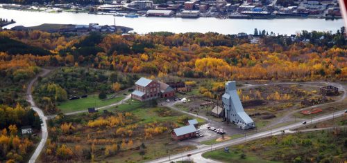 Aerial view of a landscape with colorful autumn trees, buildings, and a river in the background.