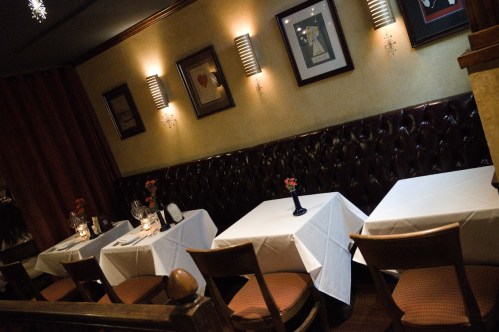 Cozy restaurant interior with white tablecloths, elegant decor, and dim lighting, featuring a tufted leather wall.