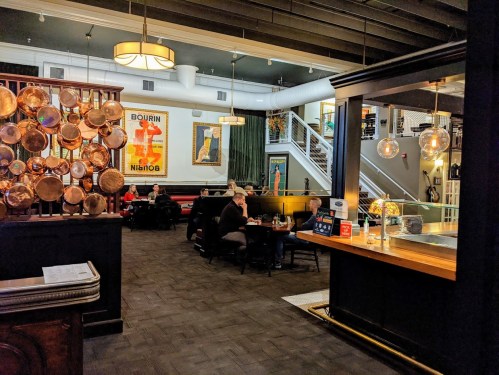 A cozy restaurant interior featuring wooden accents, copper pots, and diners enjoying meals at tables.