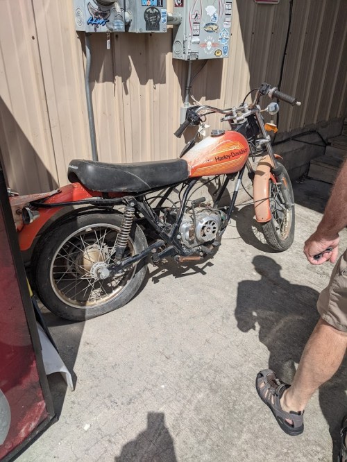 A vintage Harley-Davidson motorcycle parked beside a wall, with a person in shorts standing nearby.