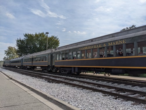 A vintage train with "Coopersville & Marne" on the side, parked on tracks beside a platform and trees in the background.