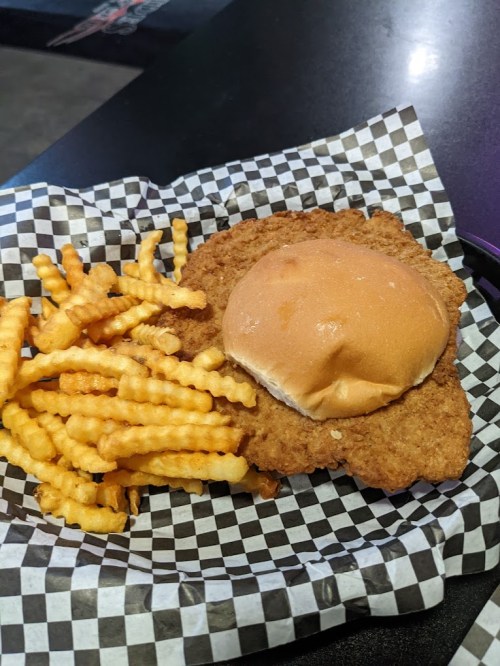 A plate with a crispy chicken sandwich on a bun and a side of crinkle-cut fries, served on checkered paper.