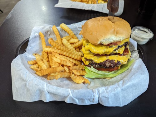 A towering cheeseburger with multiple layers of cheese, lettuce, and a side of crinkle-cut fries on a tray.