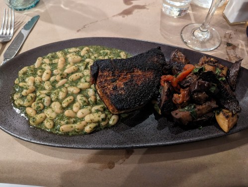 A plate featuring blackened fish, grilled meat with peppers, and a side of white beans in pesto sauce.