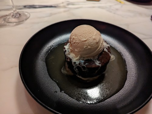 A warm chocolate dessert topped with a scoop of vanilla ice cream, served on a black plate with a drizzle of sauce.