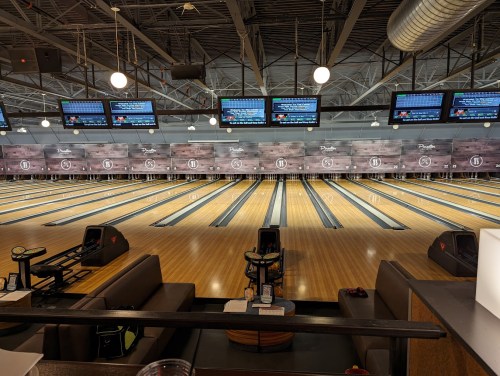 A view of an empty bowling alley with multiple lanes, seating areas, and screens displaying scores.