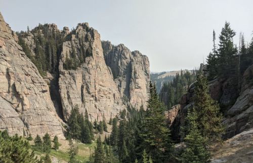 A scenic view of towering rock formations surrounded by dense evergreen trees and a hazy sky.