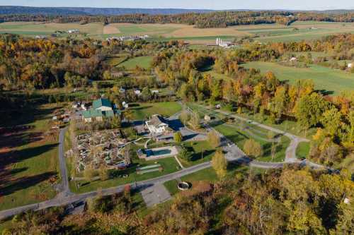 Aerial view of a rural landscape with a park, buildings, and colorful autumn trees in the background.
