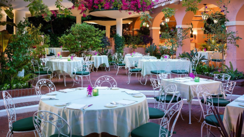 Elegant outdoor dining area with white tables, green chairs, and vibrant flowers in a lush garden setting.