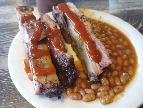 A plate of barbecue ribs drizzled with sauce, served with a side of baked beans.
