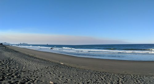 A serene beach scene with gentle waves, a clear blue sky, and distant landforms on the horizon.