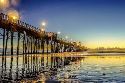 A serene sunset over a pier, with lights reflecting on calm water and a colorful sky in the background.