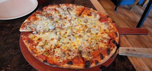 A freshly baked pizza with melted cheese, sausage, and green peppers, sliced into eight pieces on a wooden serving board.