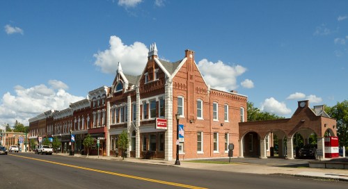 Historic brick buildings line a street under a blue sky with fluffy clouds, showcasing charming architecture.