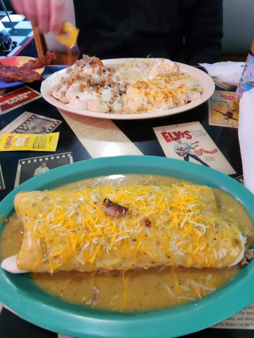 A plate of enchiladas topped with cheese and sauce, alongside a plate of rice and a side of mashed potatoes.