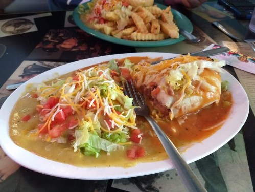 A plate of enchiladas topped with cheese and sauce, served with a side salad of lettuce, tomatoes, and shredded cheese.
