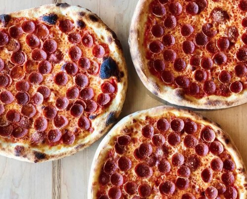 Three pizzas topped with pepperoni on a wooden table.