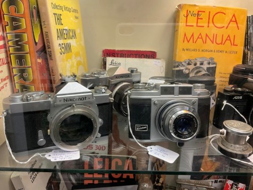 A display case featuring vintage cameras, including a Nikon and a Konica, alongside photography manuals and accessories.