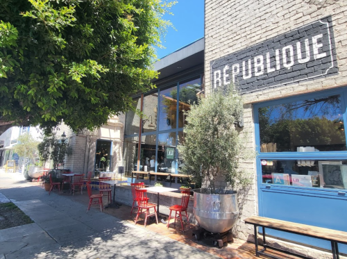 Exterior of a café named "République," featuring outdoor seating and large windows, surrounded by greenery.