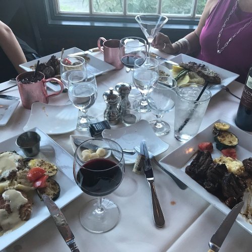 A dining table with plates of food, glasses of wine, and cocktails, set in a cozy restaurant atmosphere.