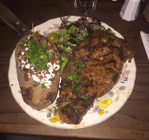 A plate featuring a grilled steak, a loaded baked potato with sour cream and chives, and a side salad.